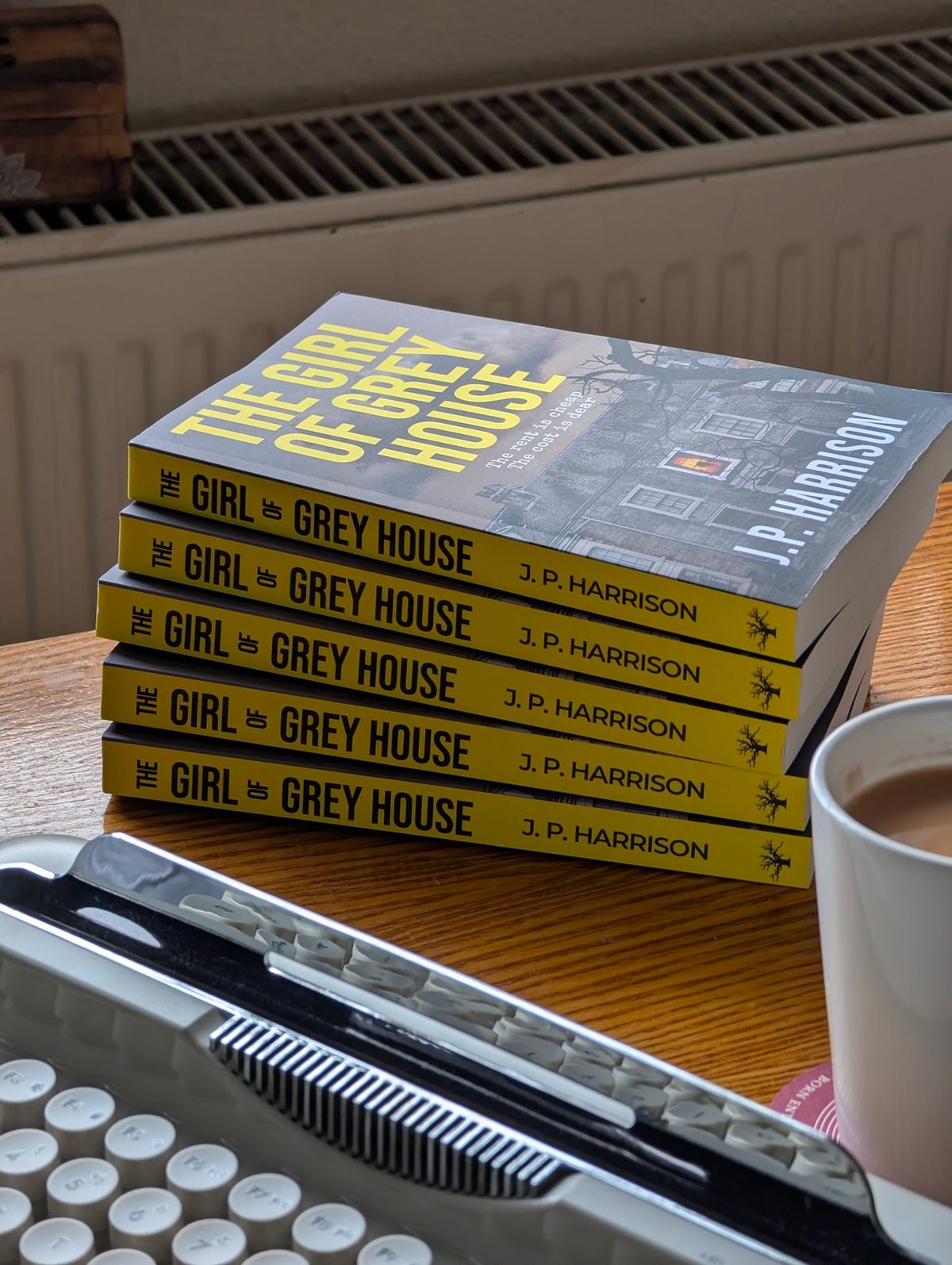 A stack of signed paperback copies of The Girl of Grey House on a writing desk